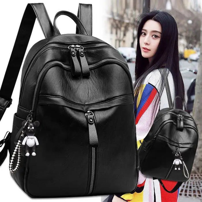 Black leather school backpack with multiple zippers and a cartoon bear charm attached.