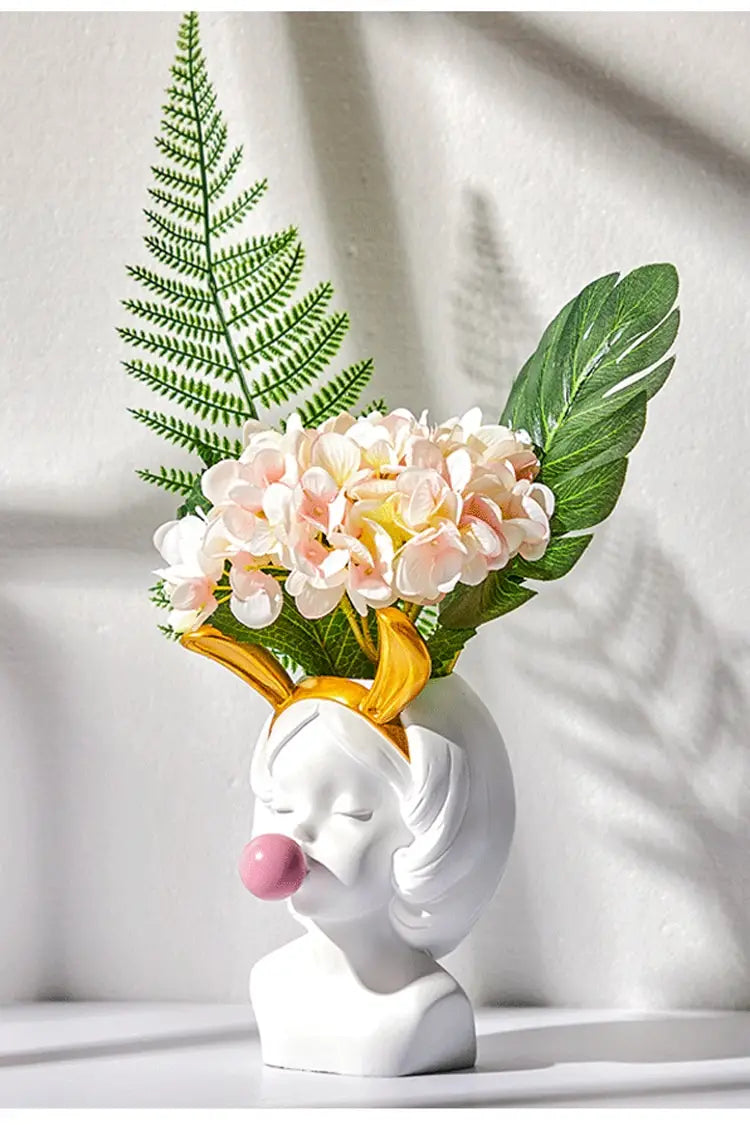 Weiße Keramikvase „Bubblegum Girl“ in Form eines Frauenkopfes mit goldenen hirschgeweihartigen Hörnern und pinkem Kaugummi im Mund, mit goldenen Akzenten.