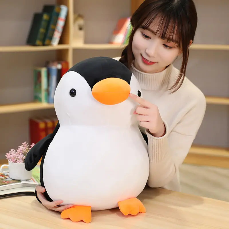 Ein Plüsch-Pinguin-Spielzeug als weiches Kuscheltier mit weißem Körper, schwarzem Kopf und Flossen sowie orangefarbenem Schnabel und orangefarbenen Füßen, entworfen für Kinder und Jugendliche