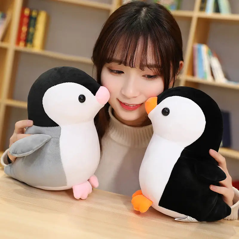 Zwei weiche Plüsch-Pinguin-Kuscheltiere für Kinder und Jugendliche: eines mit schwarzem und weißem Fell, abgesetzt mit grauen Flügeln und pinken Füßen, und ein weiteres im klassischen Schwarz-Weiß-Design mit orangefarbenem Schnabel und orangefarbenen Füßen.