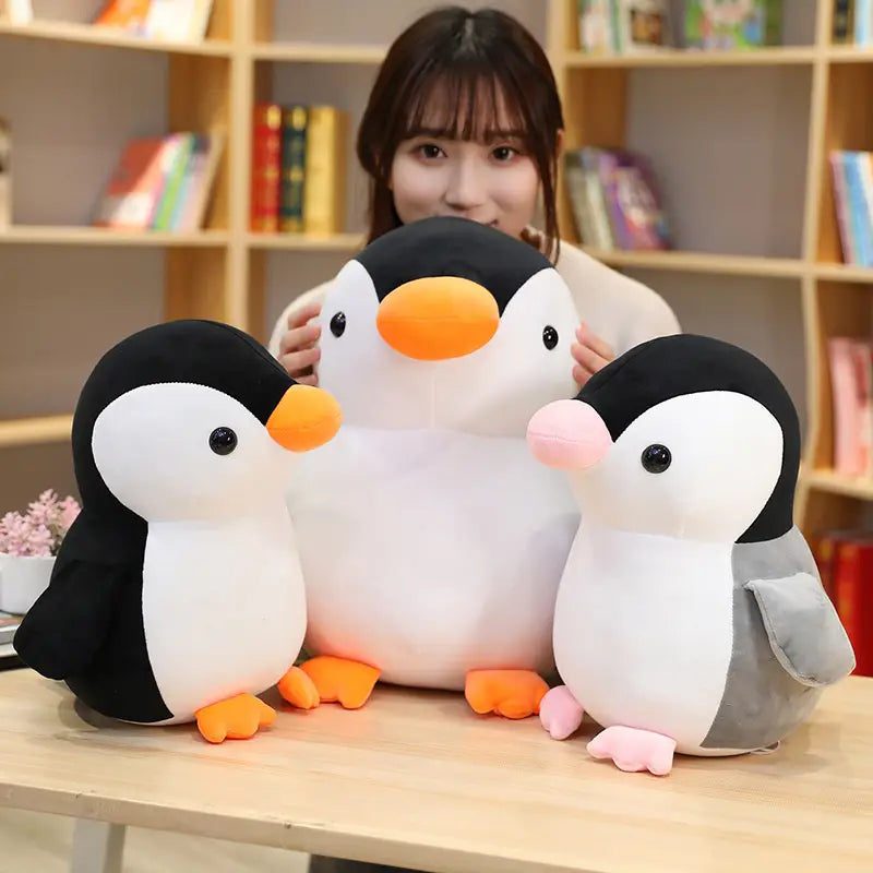 Drei weiche Plüsch-Pinguin-Kuscheltiere mit schwarzen und weißen Körpern, orangefarbenen Schnäbeln und orangefarbenen Füßen, eines mit pinken Füßen, geeignet für Kinder und Jugendliche.