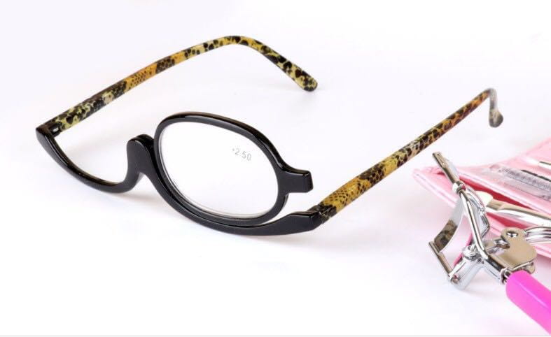Black-framed makeup reading glasses with leopard print temple arms and 2.50 strength lenses positioned next to pink nail tools on a white background.