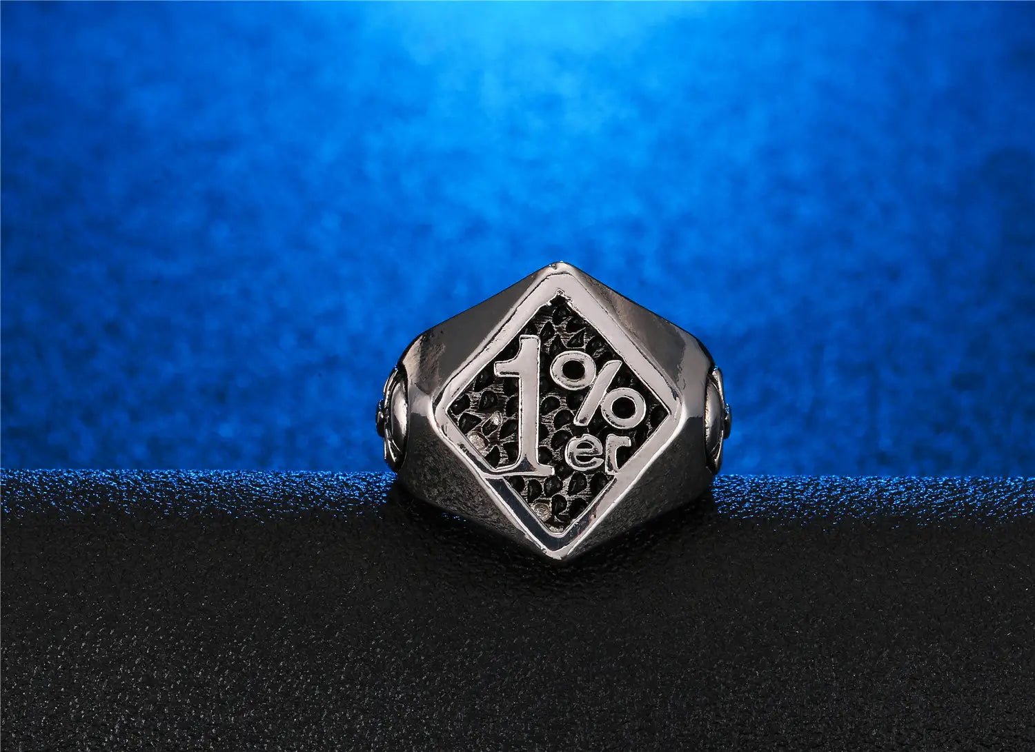 Un elegante anillo de sello de biker 1%er de acero inoxidable con acabado plateado, con cara hexagonal y diseño grabado sobre un fondo negro texturizado.