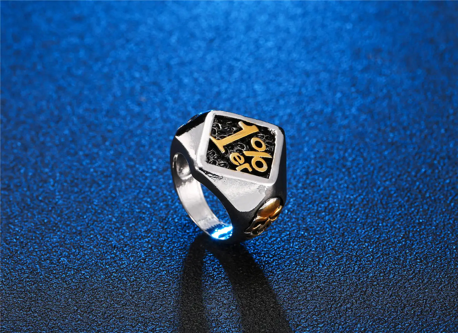 Anillo de sello de biker 1%er de acero inoxidable con acabado plateado y dorado, con incrustación negra que presenta la palabra yolo en letras estilizadas.