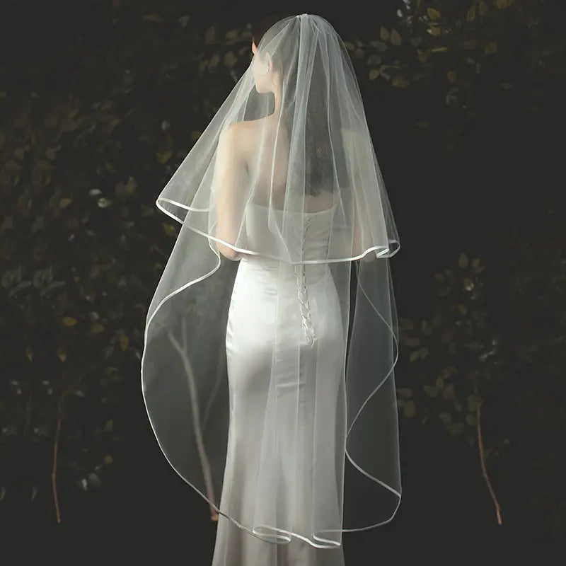 Double layer white tulle short veil with a delicate translucent fabric featuring a soft ruffled edge and subtle satin trim attached to a hair comb.