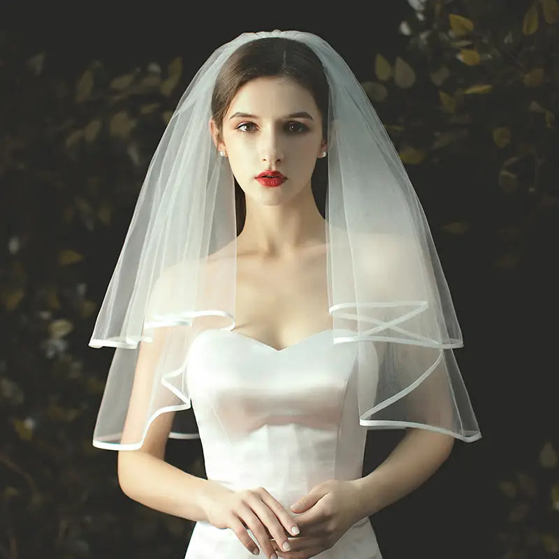 A delicate two-tiered white tulle short veil with subtle ruffled edges and a hair comb attachment.