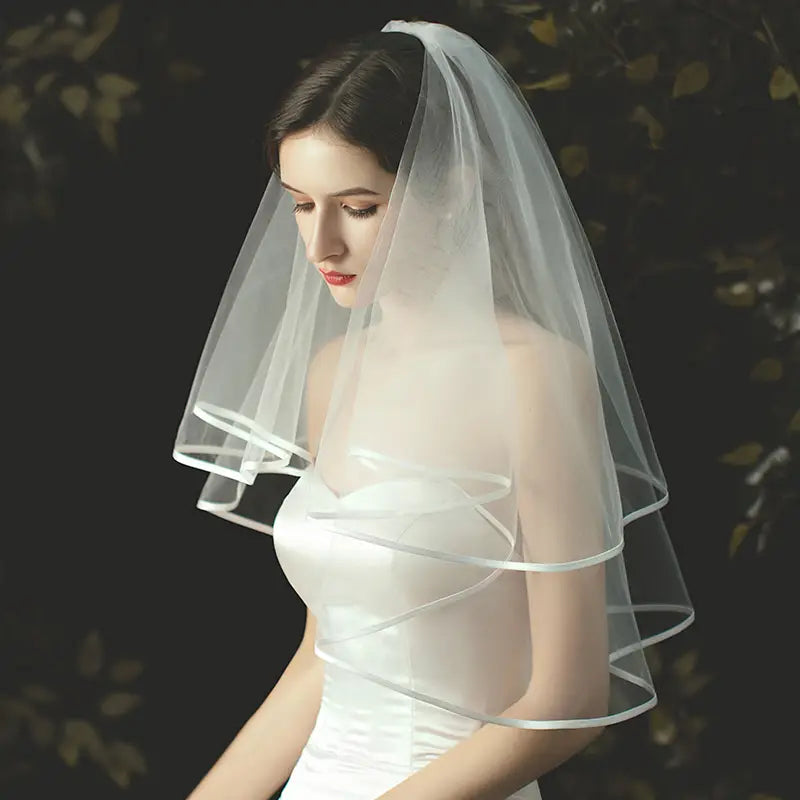 Double layer white tulle short veil features delicate translucent fabric with layered ruffled edges and a subtle sheen attached to a hair comb.