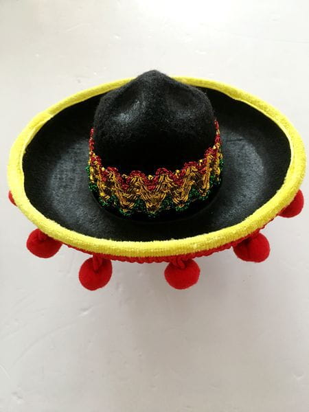 Knitted dog sombrero hat pet costume featuring a black knitted hat with a bright yellow brim, red pom-poms, and an ornate embroidered band in gold, red, and green.