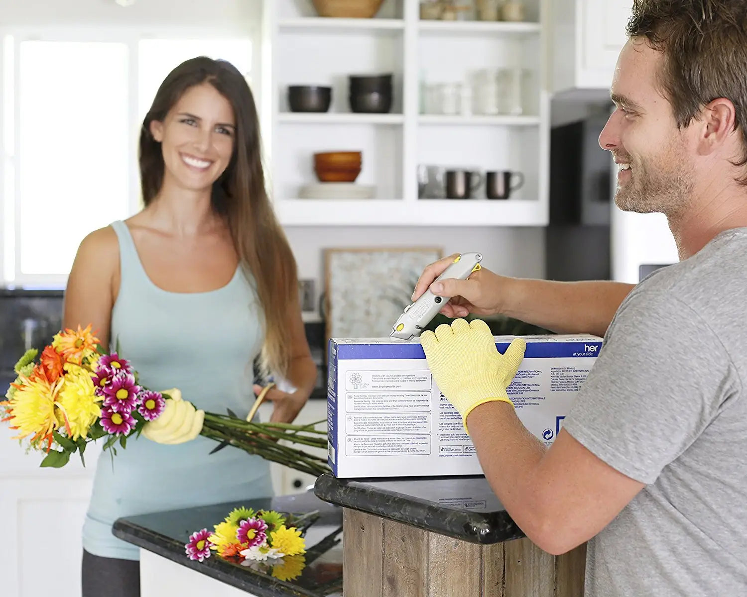 A man wearing yellow cut resistant hppe safety gloves scans a blue and white box with a handheld barcode scanner.