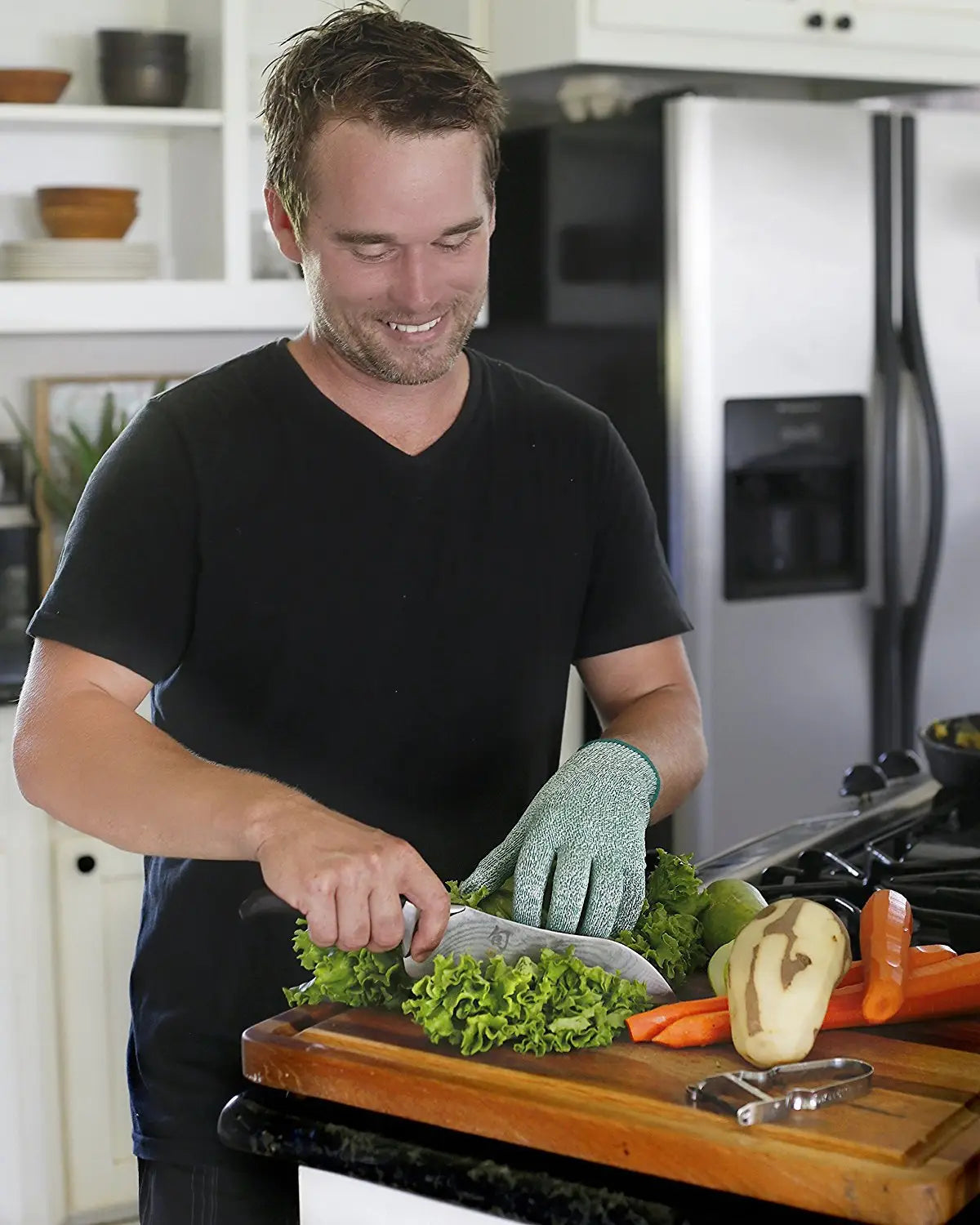 A man wearing green textured hppE cut resistant safety gloves is chopping fresh lettuce on a wooden cutting board while wearing a black v-neck t-shirt.