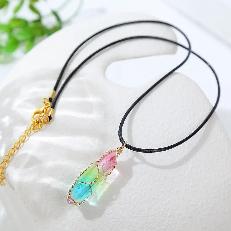 Rainbow geometric crystal wire wrapped pendant necklace featuring a colorful rainbow-hued crystal encased in gold wire wrapping and suspended from a black cord with a gold clasp.