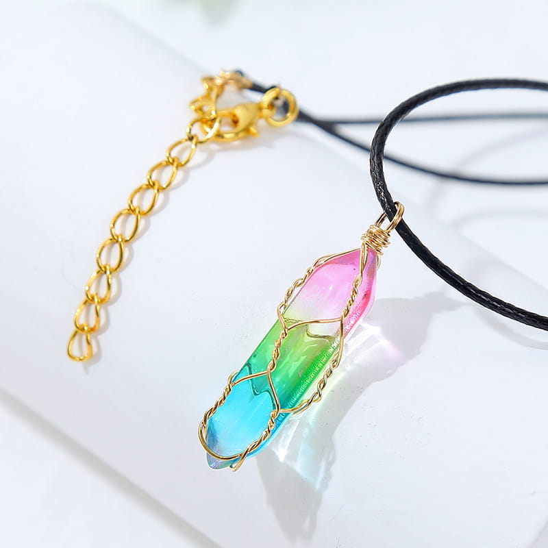 A vibrant gradient rainbow geometric crystal pendant necklace featuring a pink-to-blue color transition encased in delicate gold wire wrapping and attached to a black cord.