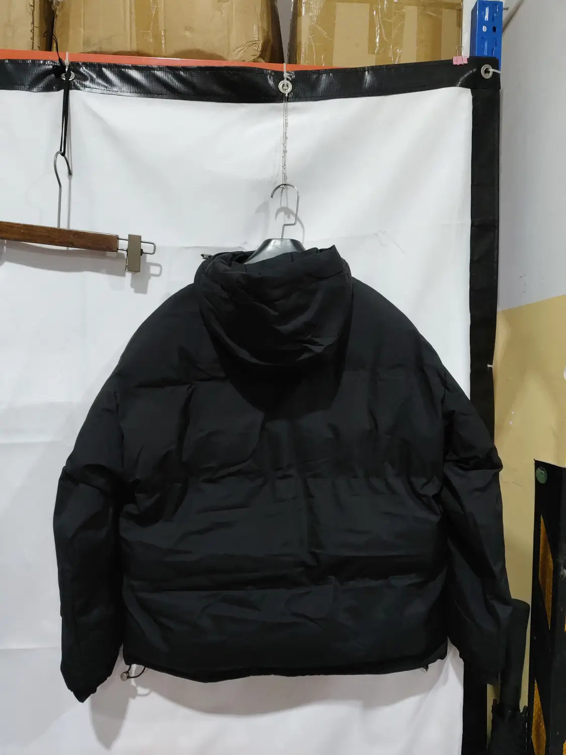 Damen-Kapuzensteppjacke mit wattierter Polsterung in Schwarz aus gestepptem synthetischem Material, gezeigt von der Rückseite.