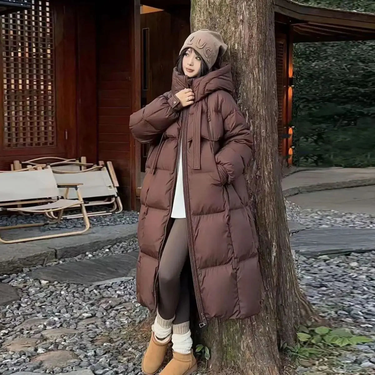 A long brown quilted puffer coat for women featuring a hood and front zipper.