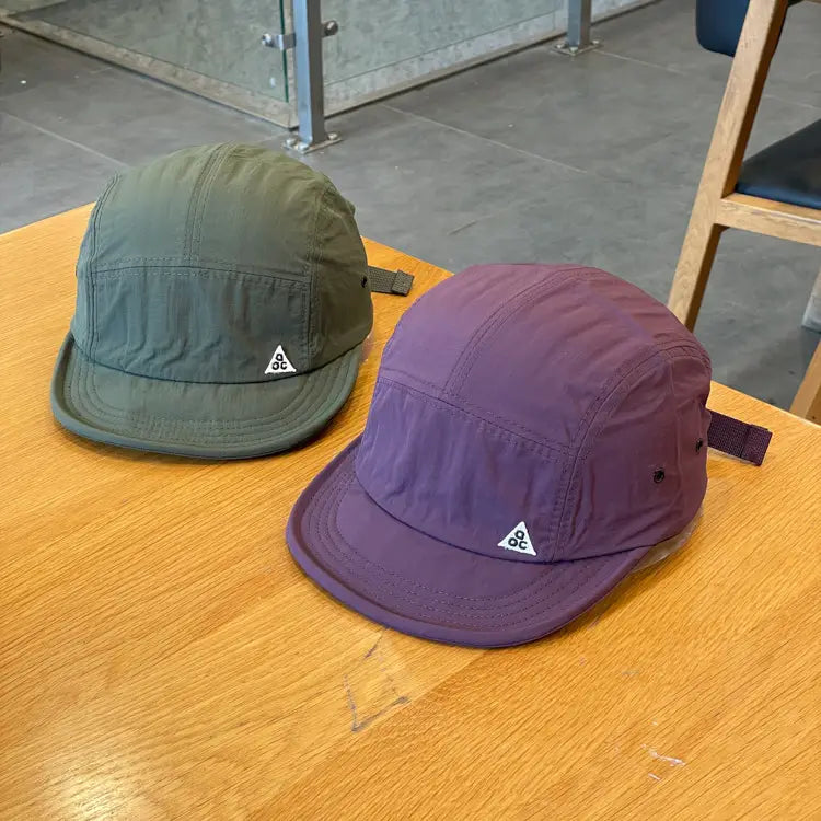 quick drying short brim five panel baseball caps in olive green and purple featuring white triangular logos on the front.