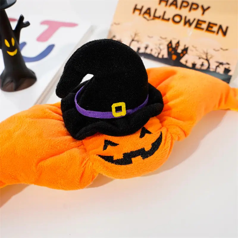 Manchon chauffant orange en peluche en forme de citrouille, avec un chapeau de sorcière noir comportant une bande violette et une boucle jaune pour un costume d’accessoire pour animal de compagnie destiné à Halloween.