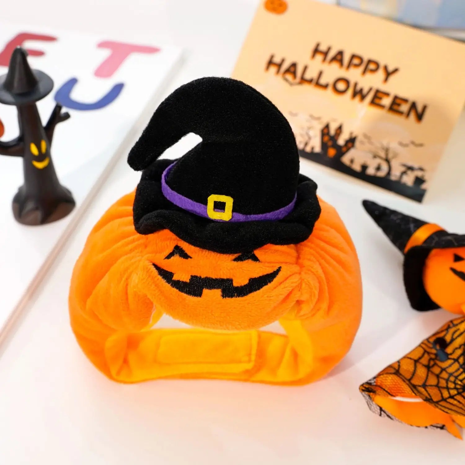 Bandeau de tête orange en peluche pour chien en forme de citrouille avec un chapeau de sorcière noir, comportant une bande violette et une boucle jaune pour un accessoire de costume pour animal de compagnie destiné à Halloween.