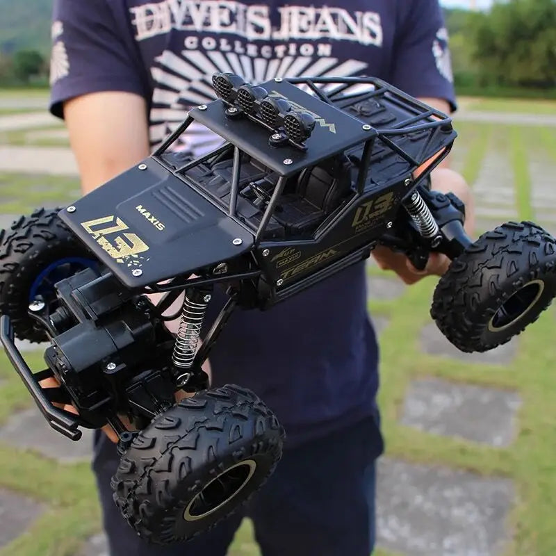 Camion teledirigido RC todoterreno 4WD de alta velocidad en negro, tipo crawler, con neumáticos resistentes y calcomanías doradas diseñadas para la escalada de rocas.