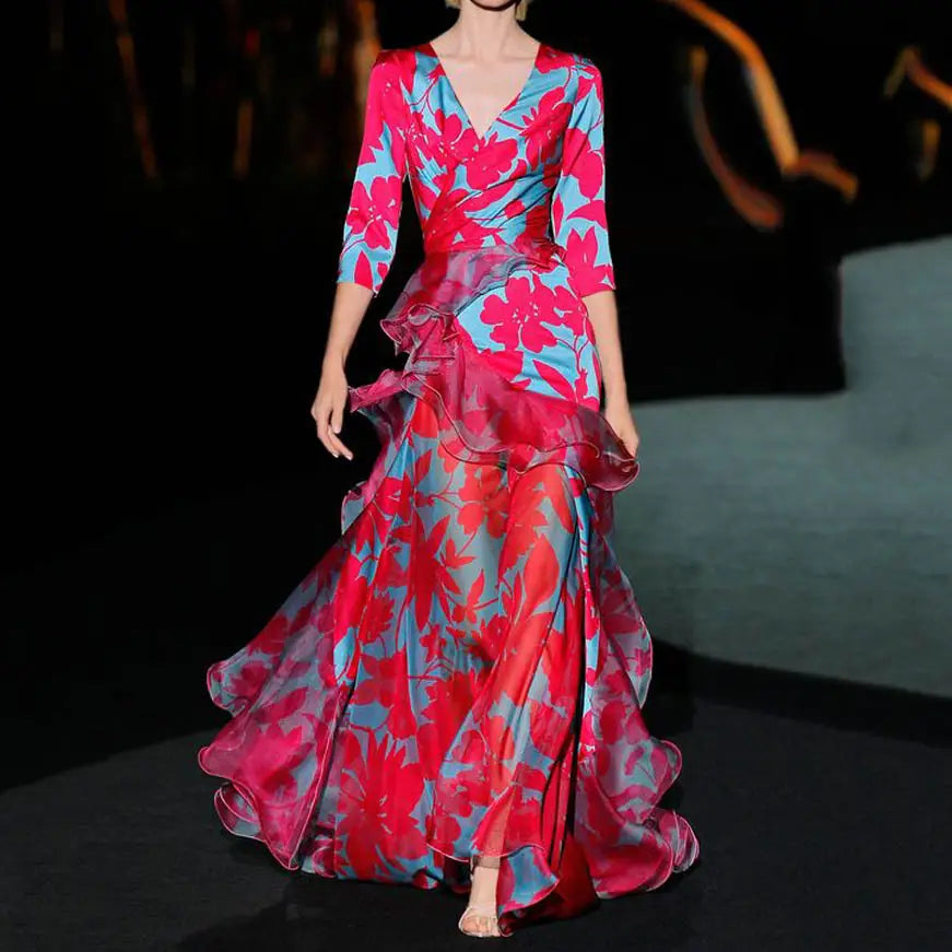 Ein fließendes Kleid im Maxilook bis zum Boden mit Blumenmuster, durchgestuften Lagen und Rüschen in leuchtendem Pink und Blau mit Blumenprint; mit V-Ausschnitt und Dreiviertelärmeln.