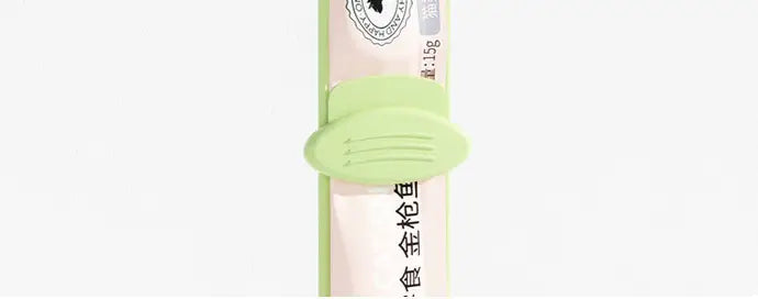 Pince en tube en silicone vert clair, munie de trois reliefs, fixant un étui cylindrique rose pâle de friandises pour chat provenant de l’ensemble « Cat Treat Squeezer and Silicone Pet Food Spoon Set ».