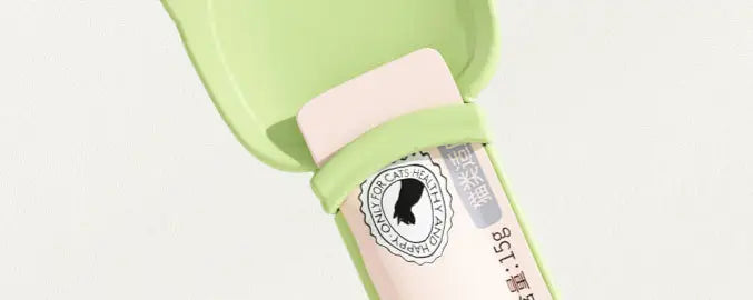 Cuillère de forme de chat en plastique vert clair, contenant une gomme rectangulaire rose avec une étiquette circulaire, dans le cadre de l’ensemble de l’extrudeuse de friandises pour chat et des cuillères en silicone pour aliments pour animaux.
