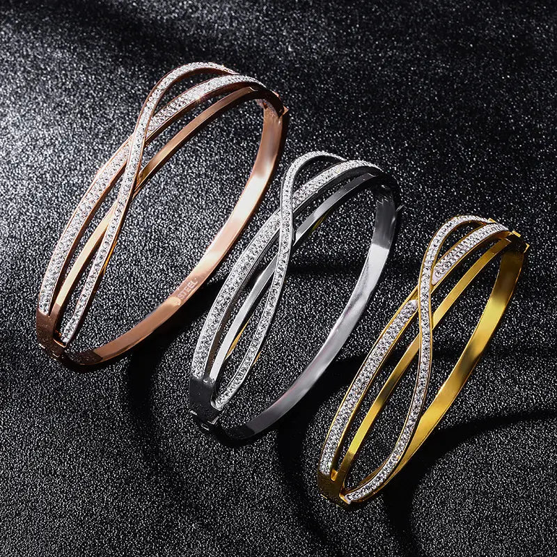 Three elegant interlocking geometric crystal inlaid titanium steel bangles in rose gold silver and yellow gold finishes each adorned with a row of sparkling clear crystals along the outer edge.