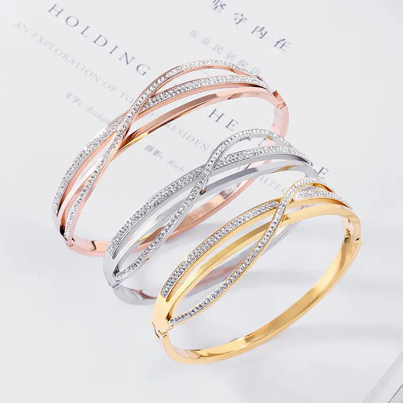 Three elegant interlocking geometric crystal inlaid titanium steel bangles in rose gold silver and yellow gold finishes each adorned with sparkling clear crystals along the bands.