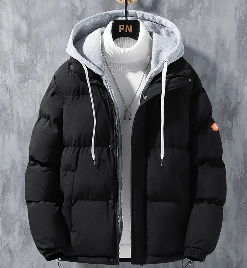 Chaqueta acolchada tipo parka impermeable y cortavientos para hombre, con capas y capucha abrigada, color negro, con capucha forrada en vellón gris, cordones blancos, diseño acolchado y logotipo circular naranja en la manga izquierda.