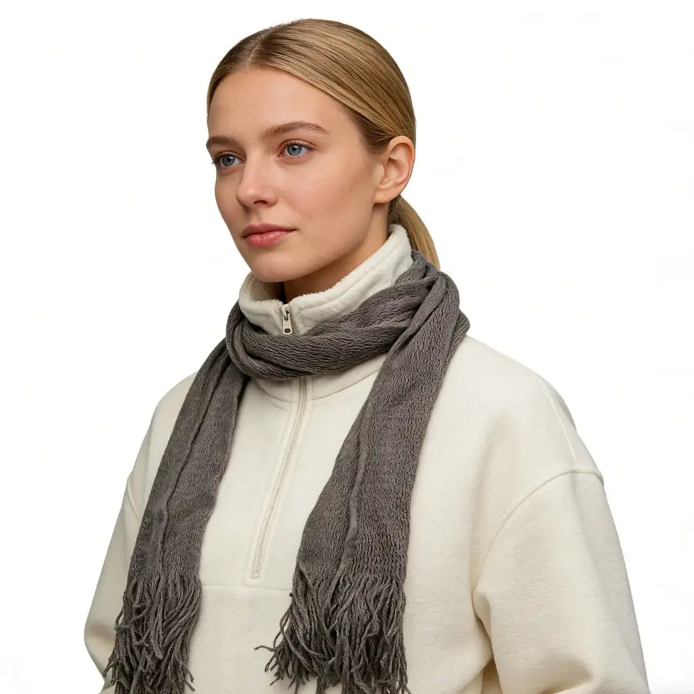 Une écharpe fine en acrylique grise douce et texturée avec des extrémités frangées, portée autour du cou comme accessoire d’hiver léger.