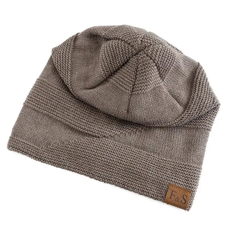 A taupe fleece lined knitted beanie cap with a ribbed brim, textured crown, and a small brown leather patch on the side.