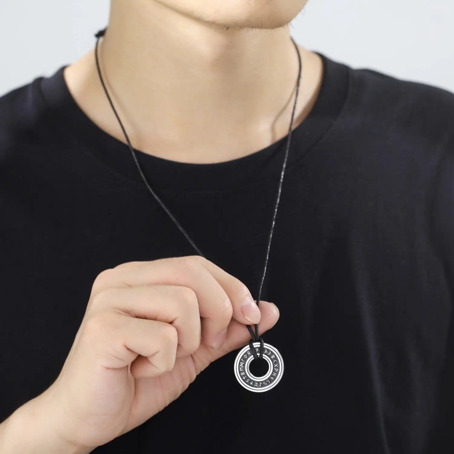 Silver circular stainless steel vintage Nordic rune pendant engraved with runes hanging from a black cord Viking necklace.