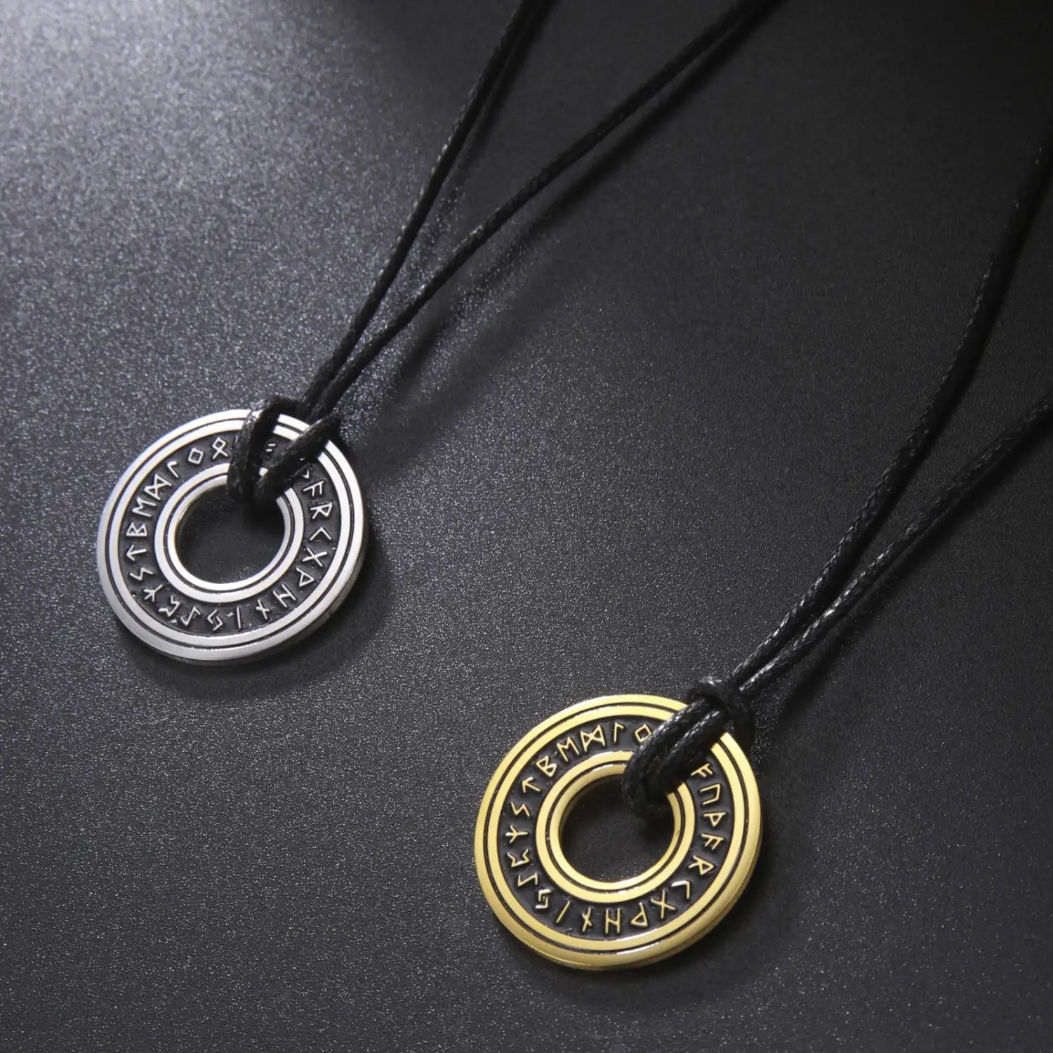 Two circular vintage nordic rune pendants in silver and gold-toned stainless steel each engraved with ancient symbols around the outer edge for a viking necklace.