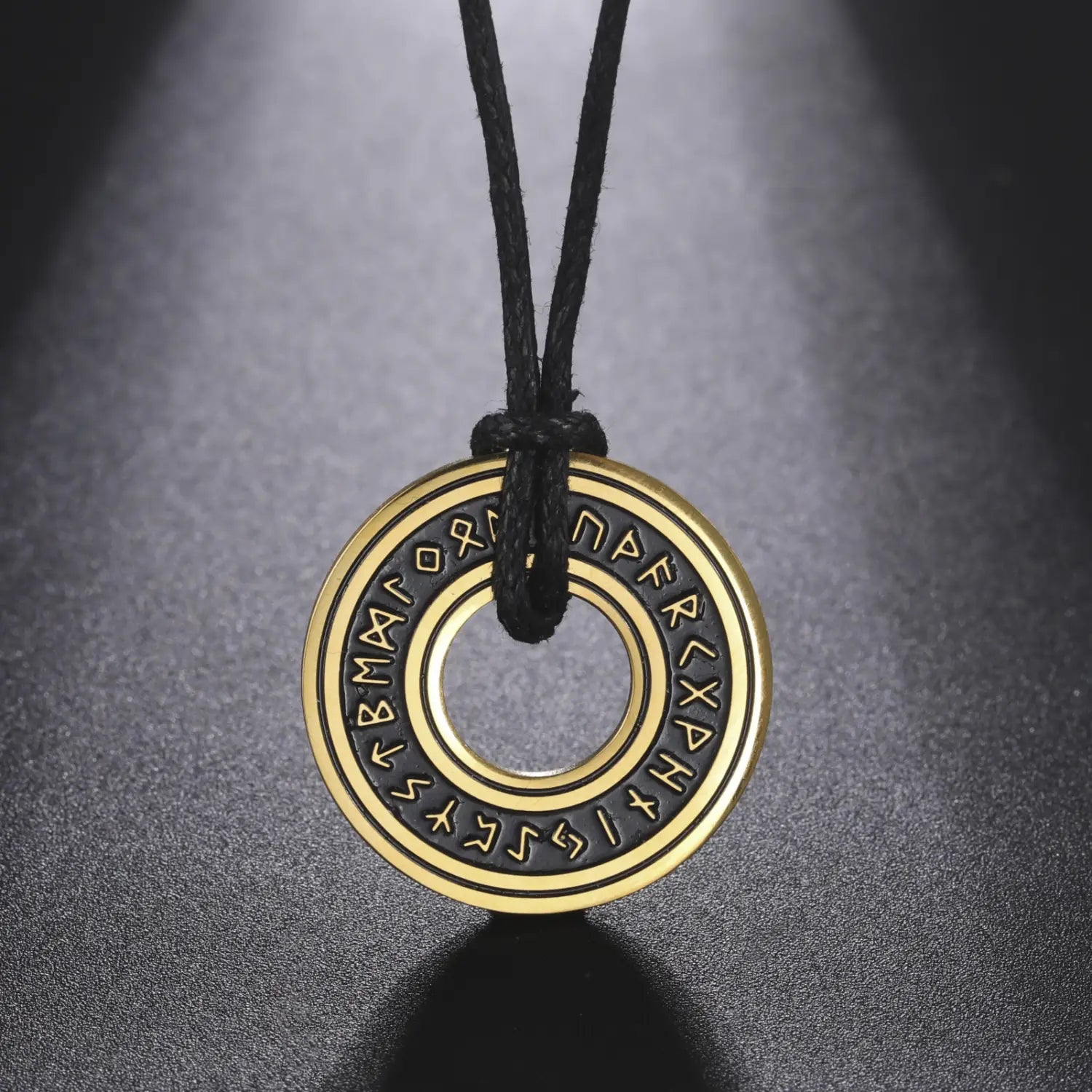 Gold-colored circular vintage Nordic rune pendant engraved with runes, made of stainless steel and suspended on a black cord as a Viking necklace.