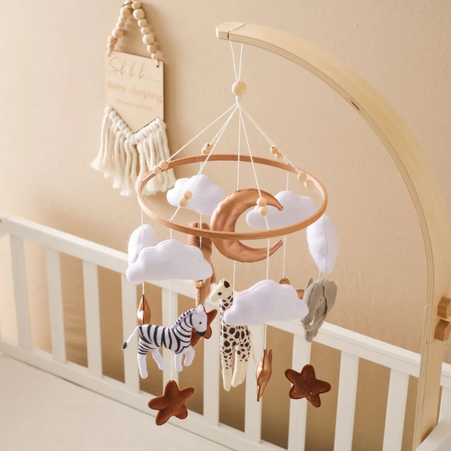 Wooden crescent moon and cloud mobile with felt safari animals and stars hanging above a crib for nursery decoration.