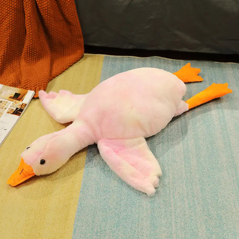 A giant white goose plush sleeping pillow toy in pink with an orange beak and feet lying on a striped rug.