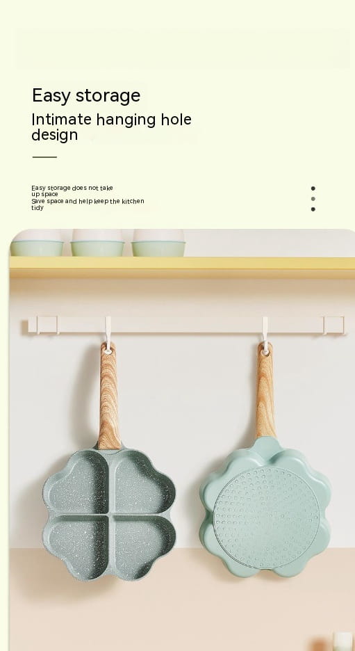 Two pastel green flower-shaped nonstick four hole egg frying pans with wooden handles hang neatly from a wall-mounted rack.