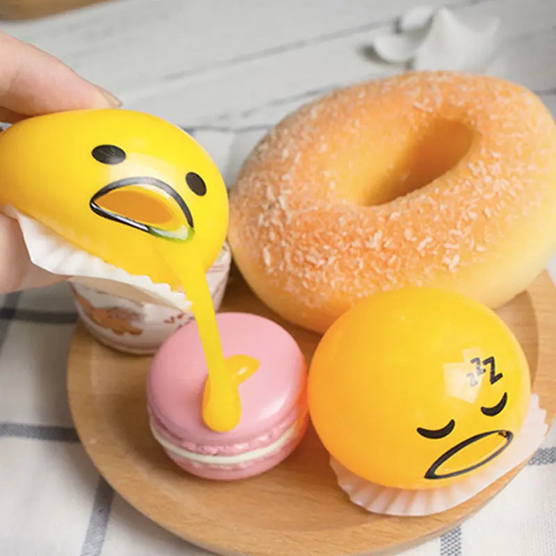 yellow gudetama egg-shaped stress ball with black facial features and a glossy finish designed as a vomiting egg yolk stress relief toy