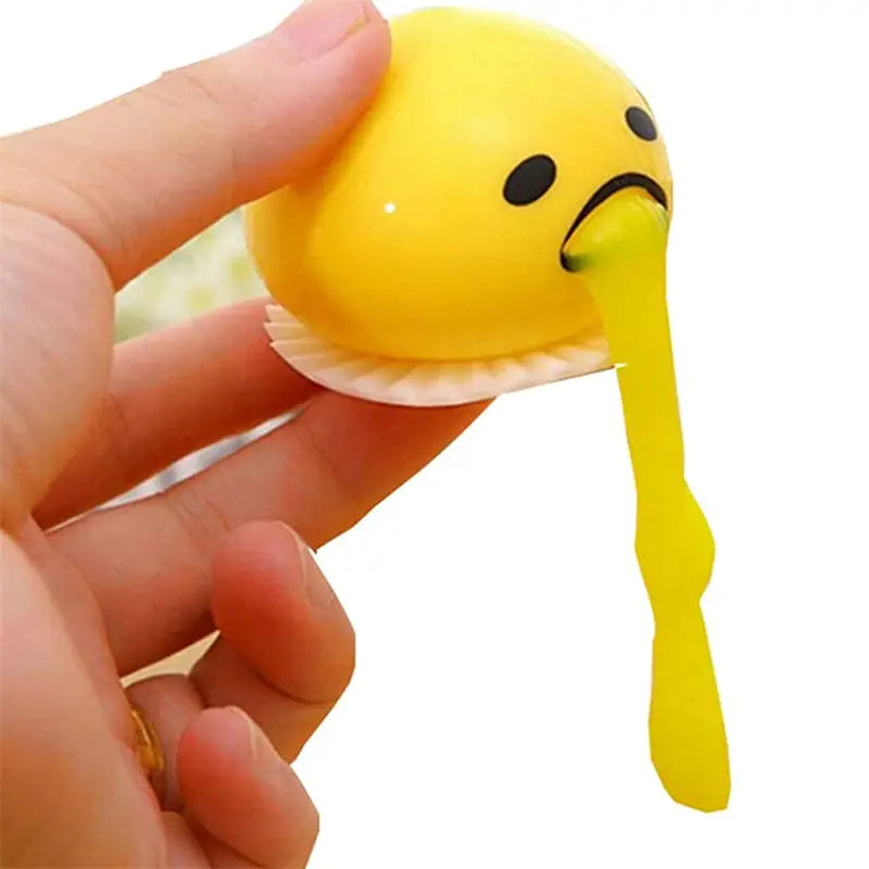Yellow Gudetama vomiting egg yolk stress relief toy shaped as a stress ball with black eyes and a frowning face featuring a gooey yellow substance oozing from its mouth.