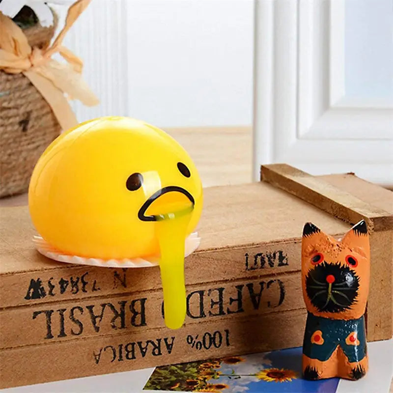 Bright yellow round Gudetama egg-shaped stress ball with a sad face and drooping expression designed as a vomiting egg yolk stress relief toy.