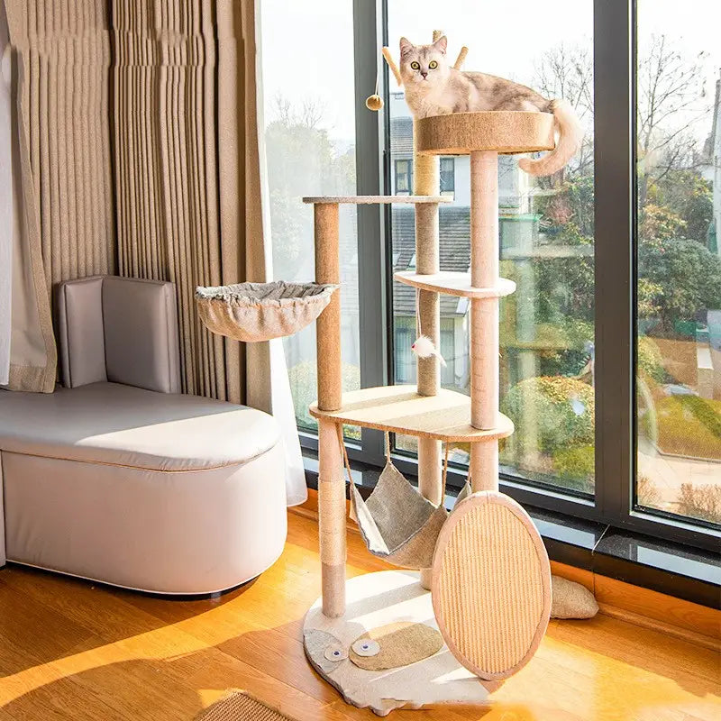 Beige large wooden cat tree climbing frame with multiple platforms scratching posts made of sisal and a hammock for cat climbing and playing.