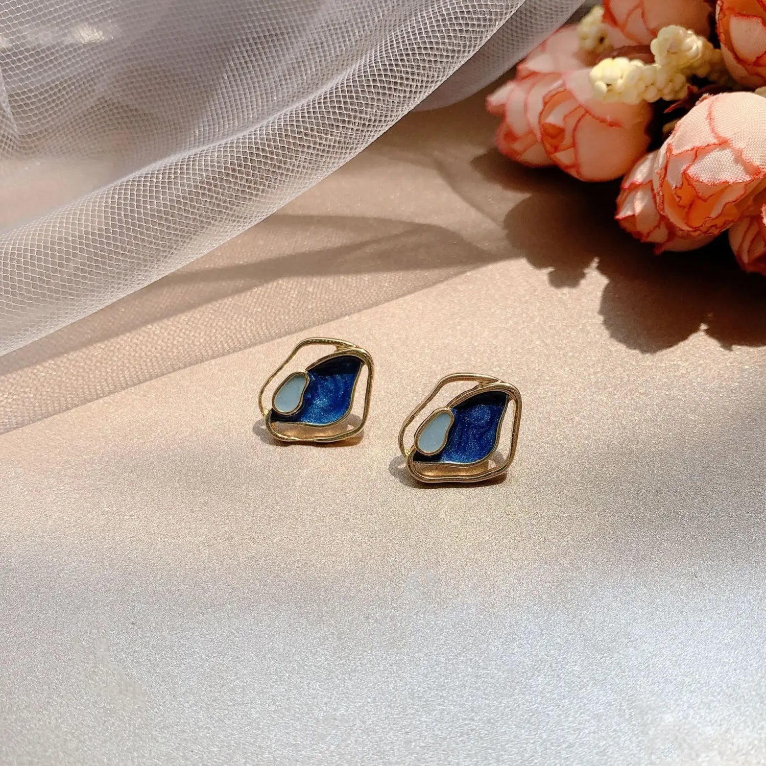 Boucles d’oreilles clous en émail bleu et bleu clair en forme de papillon, avec montures en métal de ton doré, arborant un motif géométrique en argent.