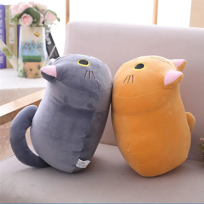 Jouet en peluche d’animal rembourré sous forme de coussin pelucheux de chat gras en gris et orange, avec oreilles internes roses, yeux noirs soulignés de jaune, moustaches cousues en pointillé, et tissu doux en velours.