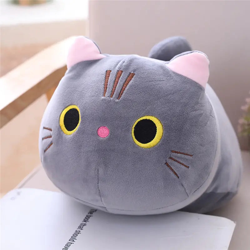Un doux coussin pelucheux gris de chat gras avec oreilles internes roses, yeux noirs bordés de jaune et un tout petit nez rose, conçu comme un jouet en peluche d’animal rembourré