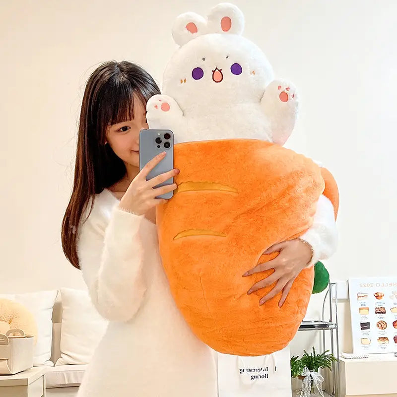 A plush white radish rabbit pillow with purple eyes and pink inner ears sitting atop a large orange carrot-shaped stuffed toy.