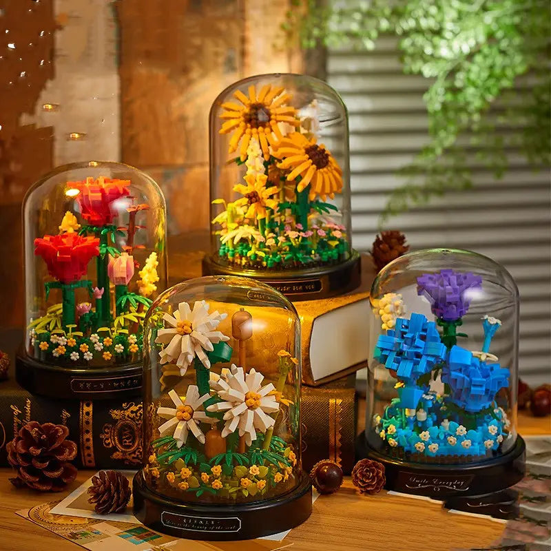 Cuatro vitrinas con cúpula de vidrio, cada una con un ramillete colorido de piezas de construcción florales bajo una disposición intrincada de flores tipo lego y plantas en miniatura.