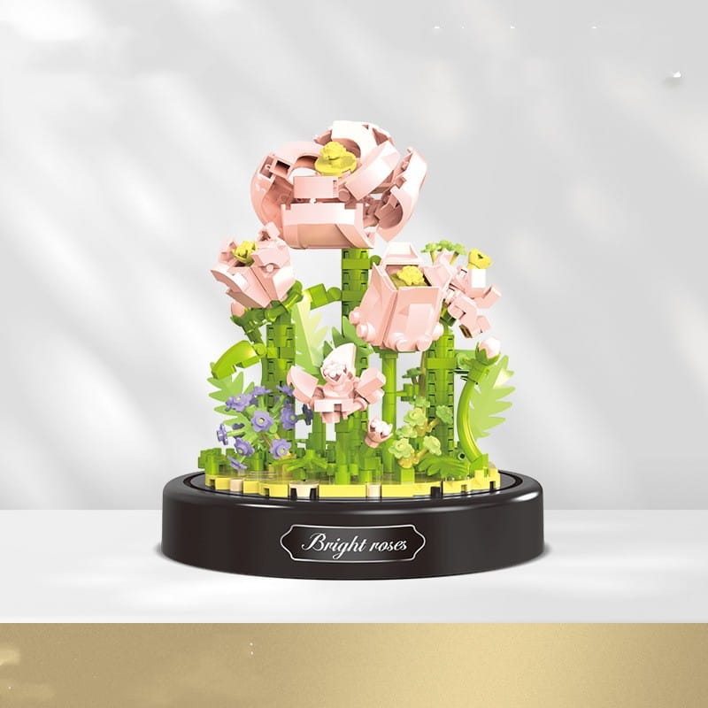 un delicado centro floral de estilo lego rosa y verde con una base negra, inscrito con rosas brillantes, en un ramillete de piezas de construcción florales bajo una cúpula de vidrio
