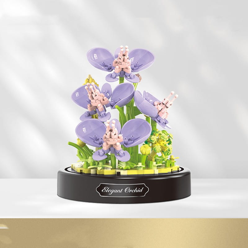 Ramillete de piezas de construcción florales en cúpula de vidrio que presenta una delicada escultura de orquídea lavanda, con centros rosas y tallos verdes, elaborada con ladrillos de plástico entrelazados sobre una base circular negra grabada con una orquídea de trazo elegante.