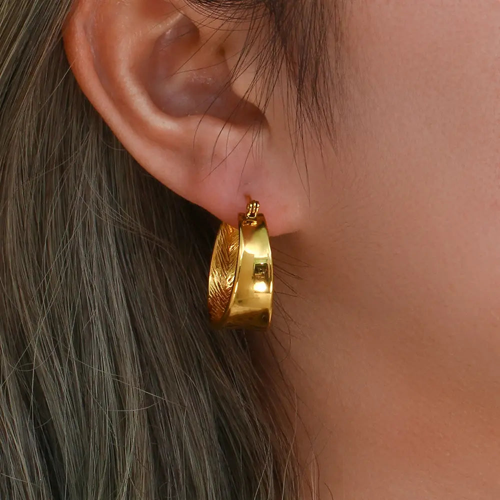 Boucles d’oreilles créoles en or avec un motif intérieur texturé en forme de plume, une finition dégradée ton sur ton et une petite touche rectangulaire.