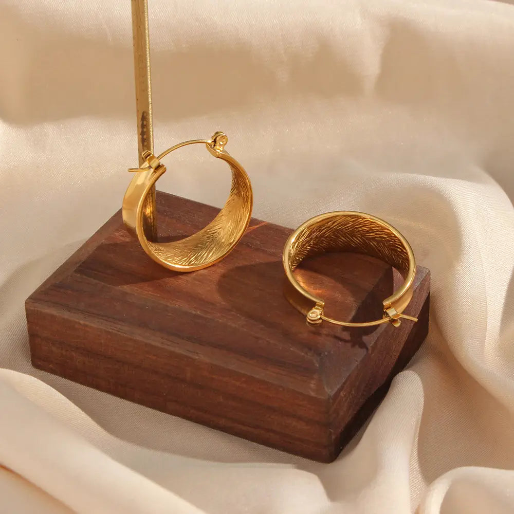 Boucles d’oreilles créoles dorées à dégradé intérieur façon plume, avec une finition or polie et un motif évoquant une plume.