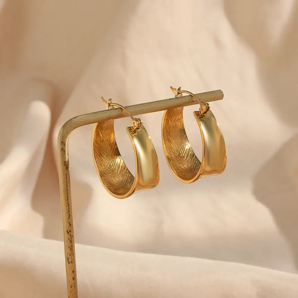 Boucles d’oreilles créoles dorées à dégradé intérieur façon plume, avec des bords extérieurs lisses et un motif évoquant une plume sur la surface intérieure.